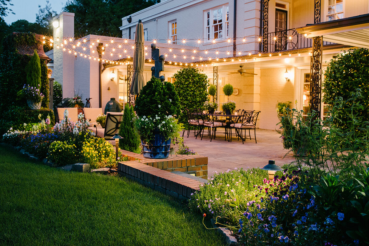 Evening outdoor setting with string lights, garden, and patio furniture.