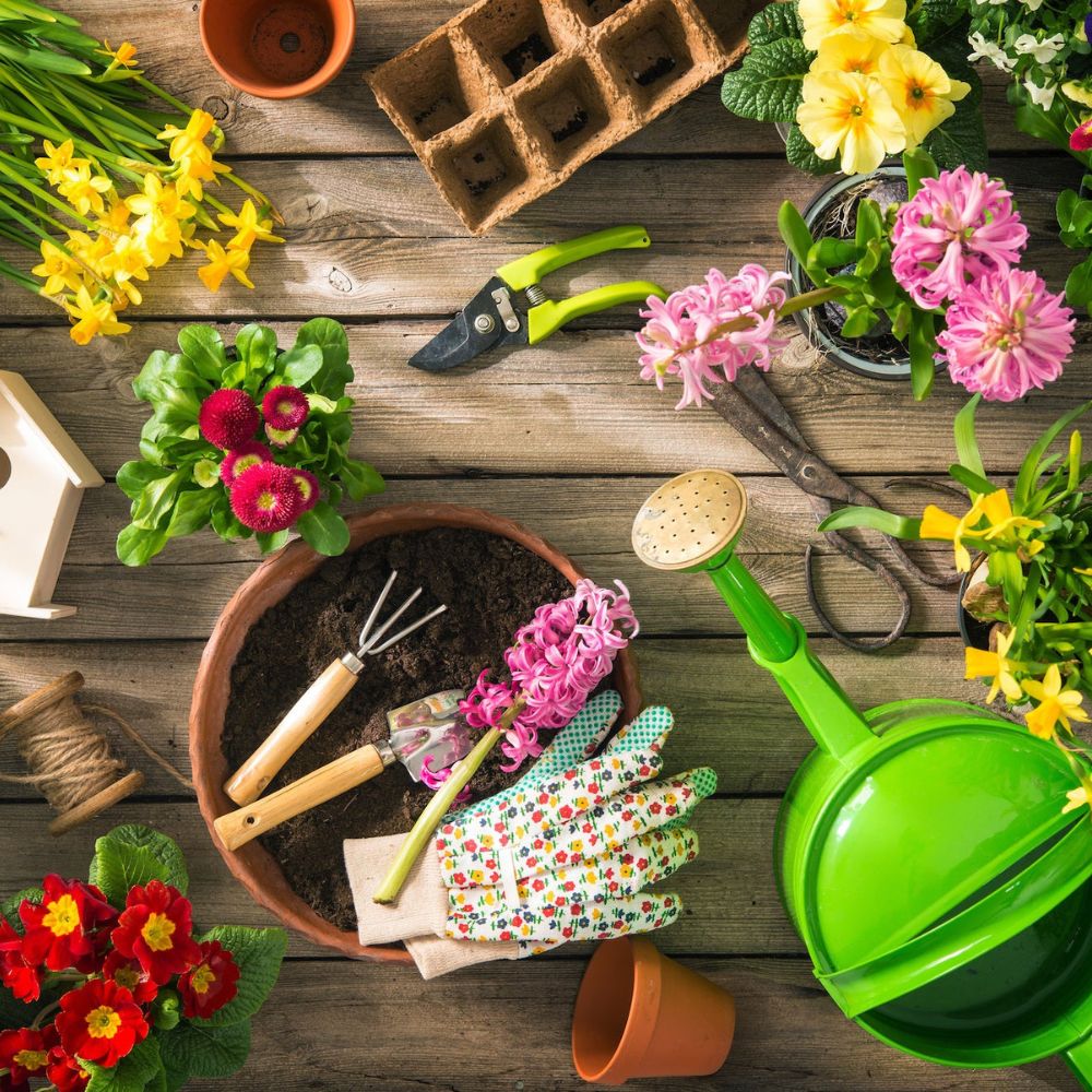 Gardening tools and supplies on a wooden table with flowers.